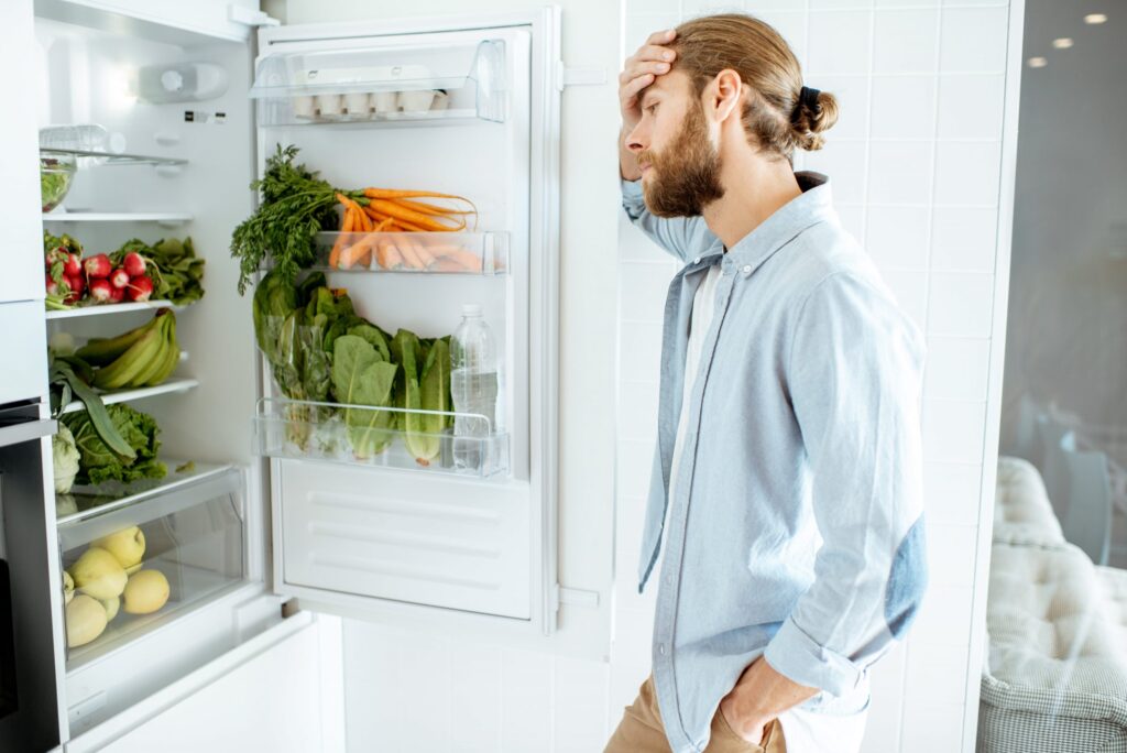 sad man near the refrigerator full of vegetables